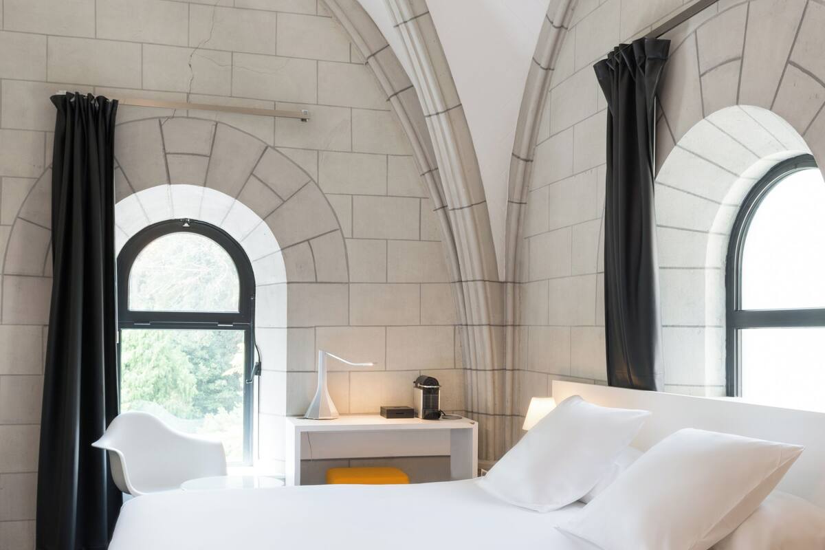 Un dormitorio moderno con una cama grande, un escritorio y dos ventanas con cortinas.