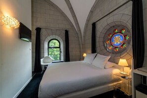 A hotel room with a large bed, a TV, a small table with a lamp, and a stained glass window with a logo. - Sozo Hotel (Nantes)