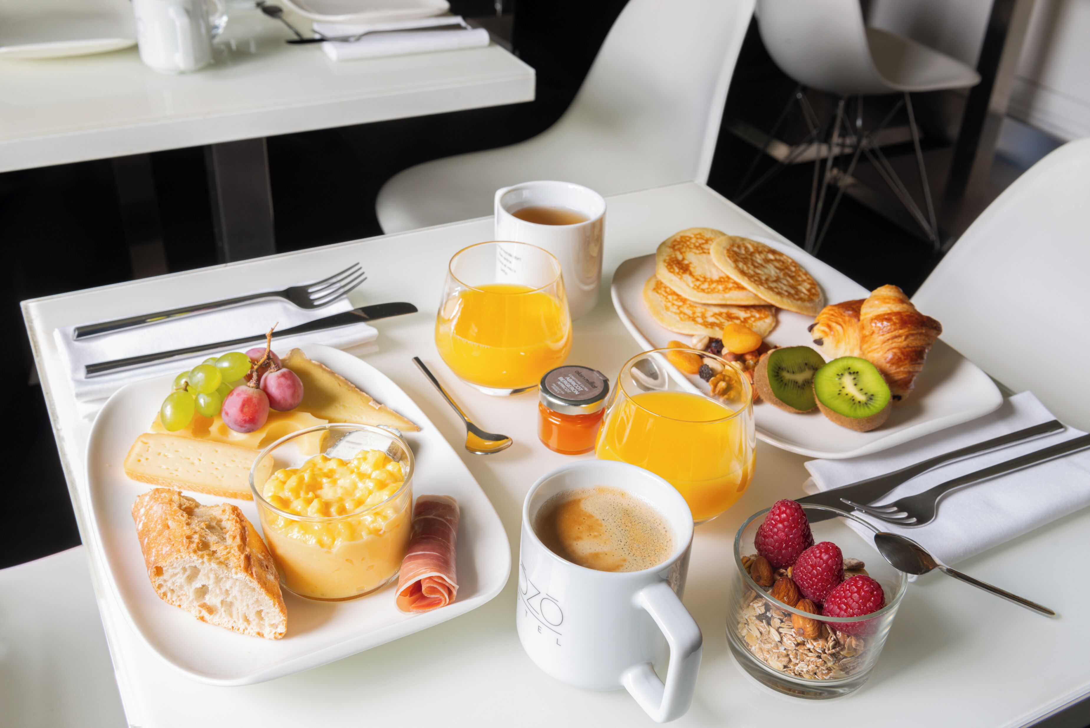 Una tavola imbandita per la colazione con croissant, pancake, frutta e una tazza di caffè.