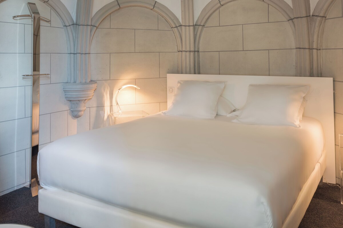A modern bedroom with a large bed, arched ceiling, and a wall-mounted light fixture.