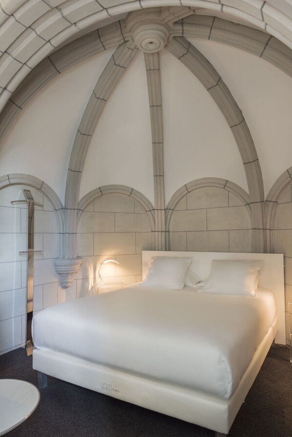 A modern bedroom with a large bed, arched ceiling, and a minimalist design.