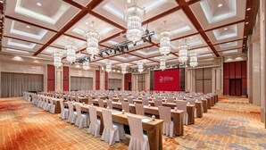 Un amplio salón de conferencias con filas de mesas y sillas, candelabros y una alfombra estampada.