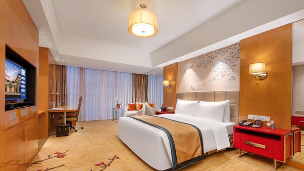 A hotel room with a large bed, a desk, a chair, a TV, and a red nightstand. - WorldHotel Grand Juna Wuxi (Wuxi)