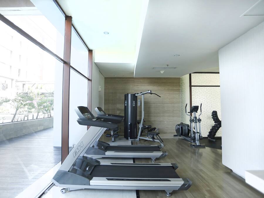 Une salle de sport moderne équipée de tapis de course, d’appareils de musculation et dotée d’une grande fenêtre donnant sur une cour intérieure.