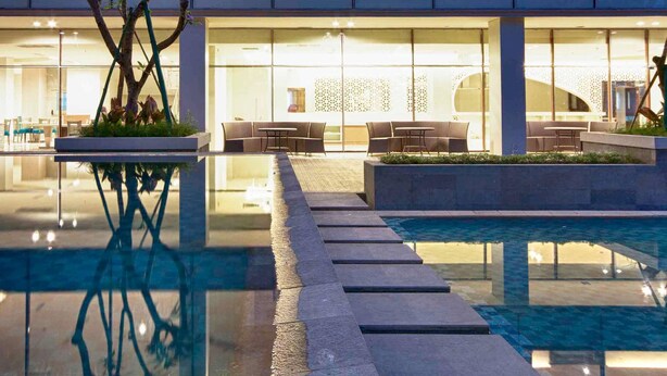 A modern outdoor pool area with a glass barrier, seating, and a reflection pool. - Mercure Padang (Padang)
