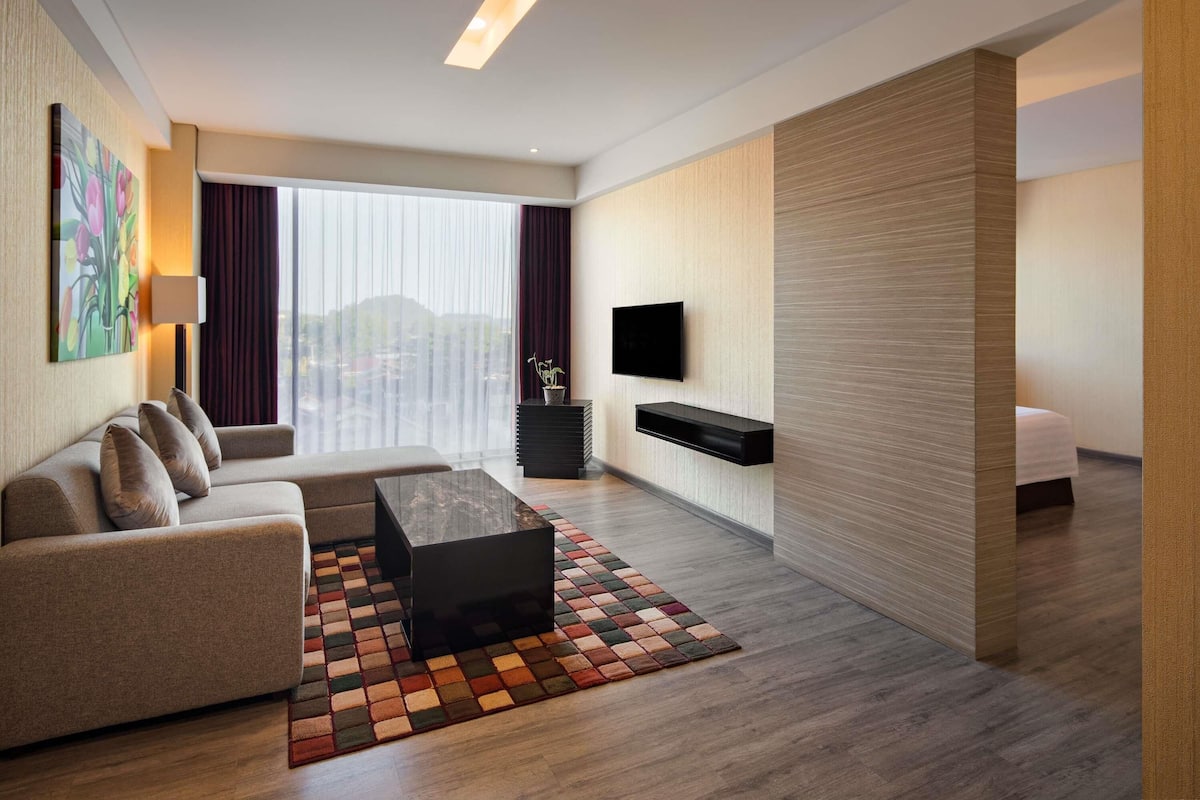 Una habitación de hotel moderna con sofá, mesa de centro, televisión y vistas a la ciudad.