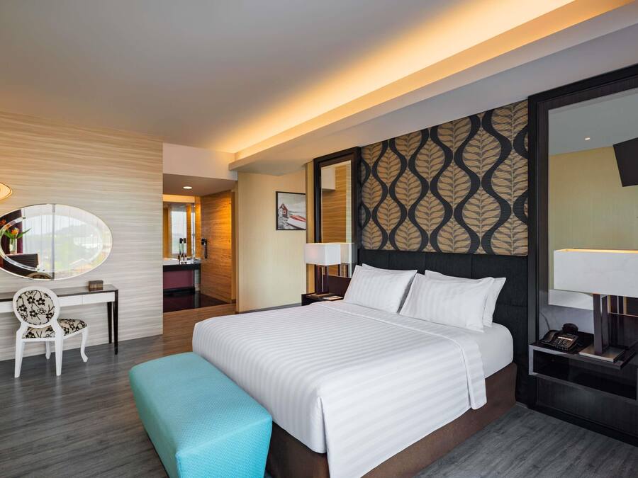 A modern hotel room with a large bed, a desk with a chair, a mirror, and a bathroom visible through an open door.