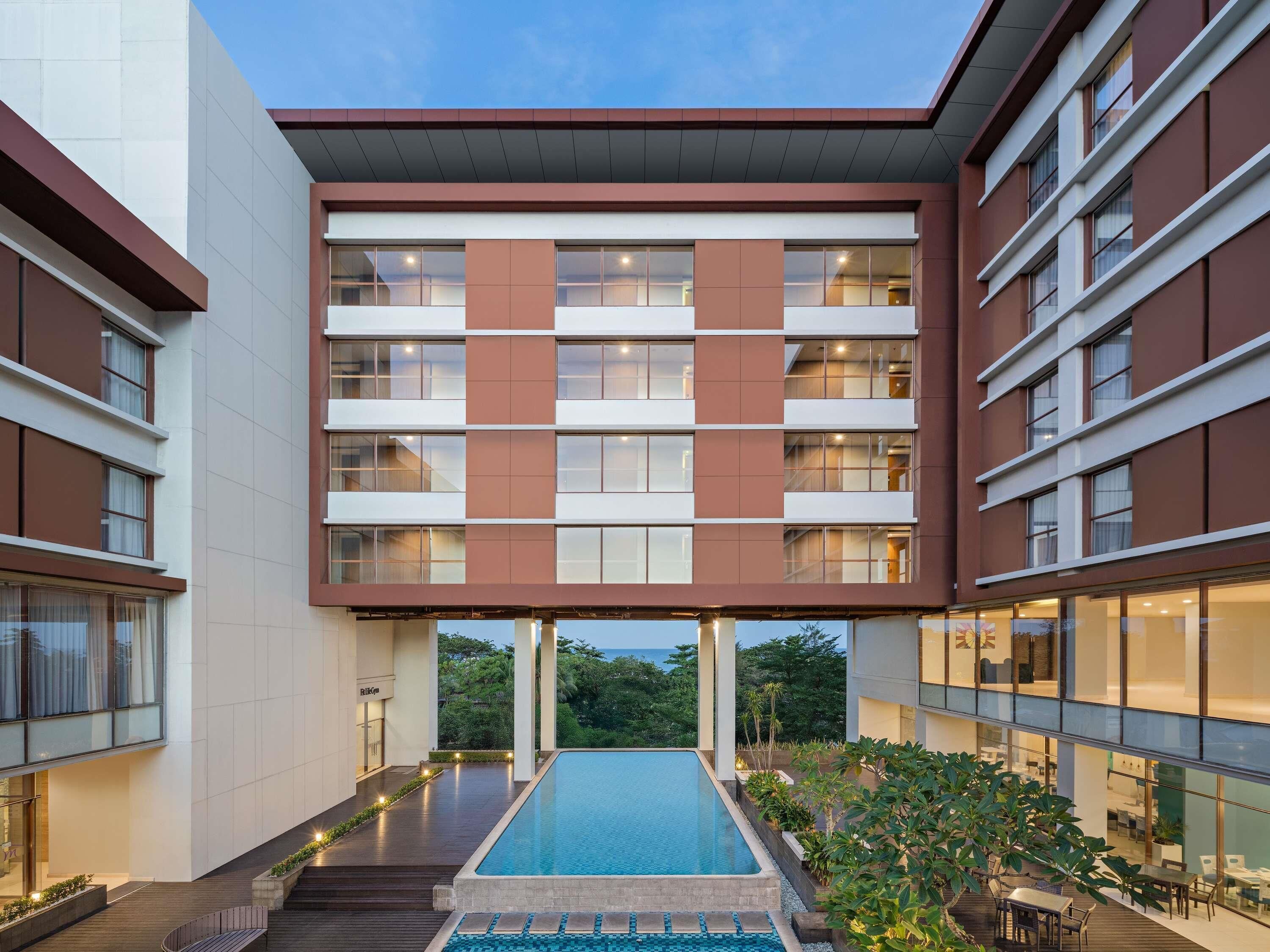 A modern hotel with a central pool, multiple floors, and a view of the sea.