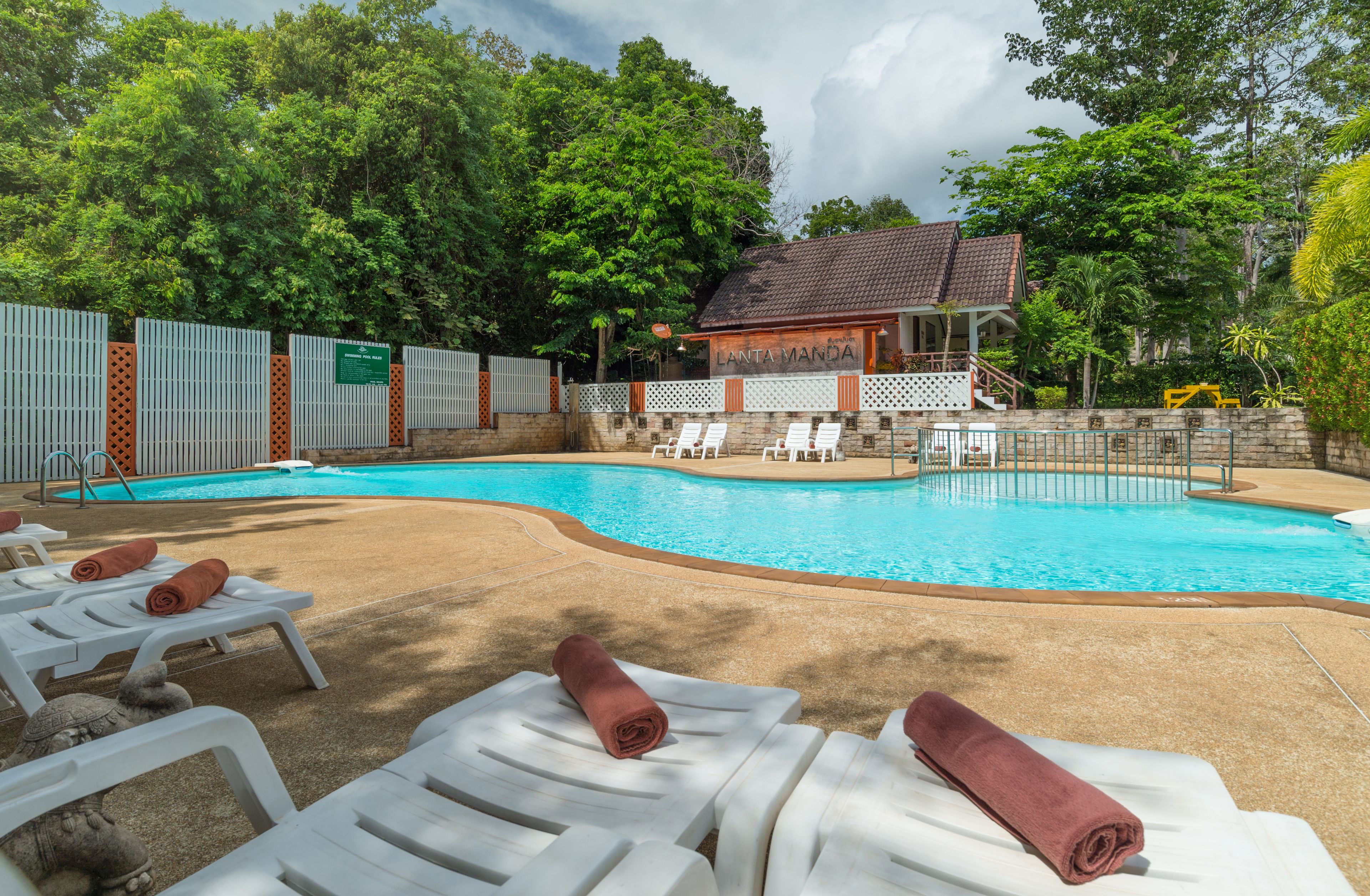 A swimming pool with lounge chairs and a building labeled "LANTA MANDRA" in the background.