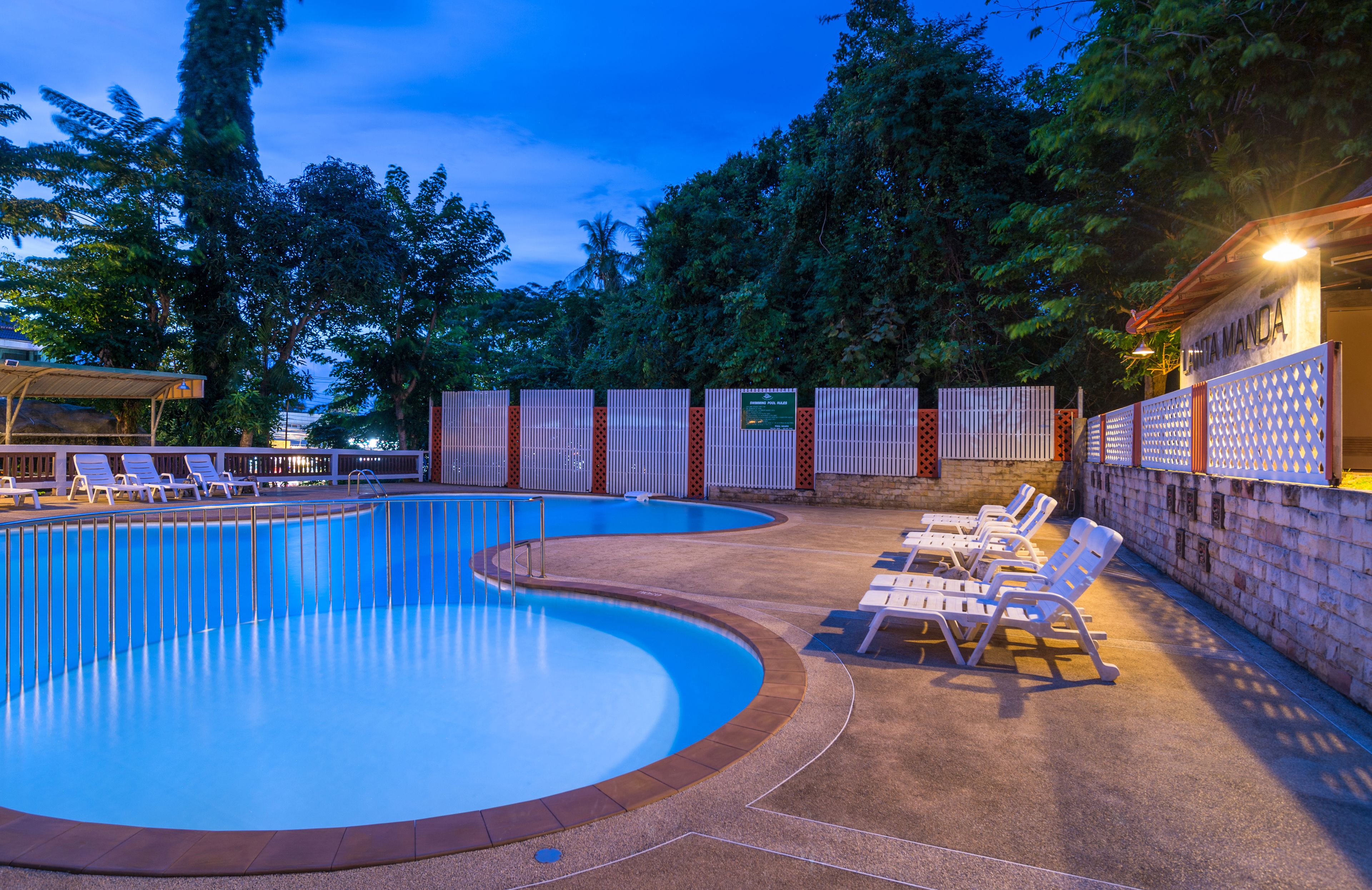 A swimming pool with lounge chairs and a covered area, surrounded by trees and a brick wall.