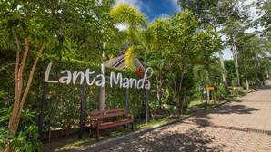 Placa com a inscrição 'Lanta Manda', um banco e um caminho.