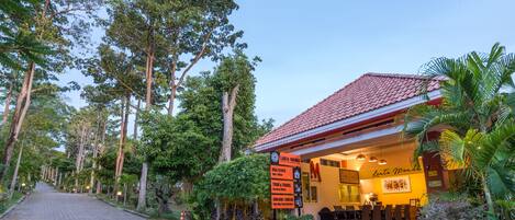 A hotel with a red tiled roof, a reception area with a 'Lanta Manda' sign, and a paved walkway lined with trees.