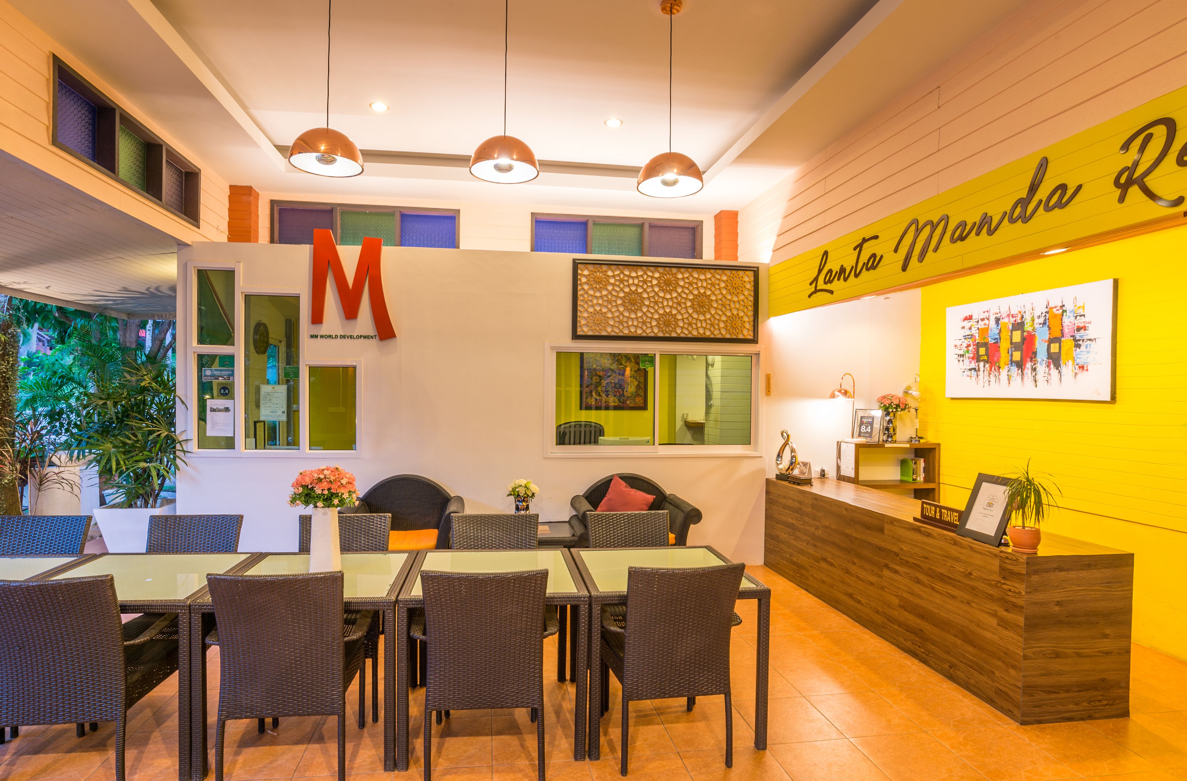 A reception area with a wooden reception desk, a large 'M' on the wall, and a glass-top table with chairs.