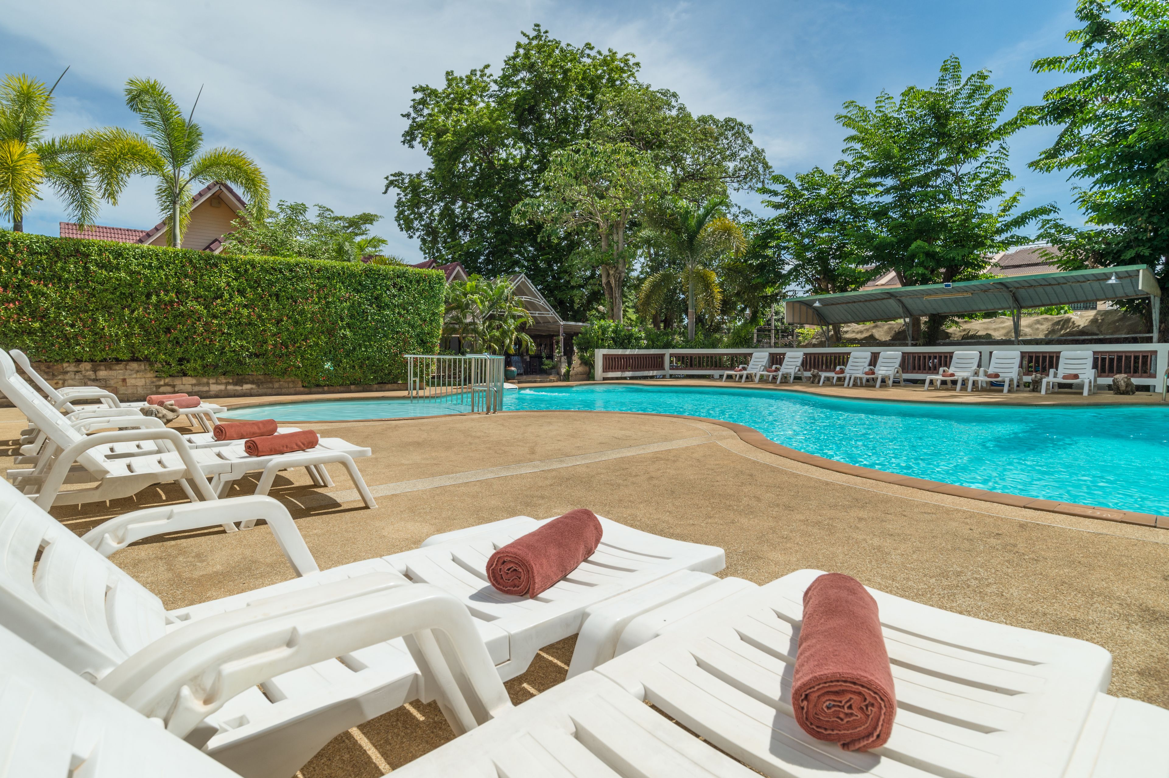 A poolside area with white lounge chairs, some with towels, and a clear blue pool surrounded by greenery.