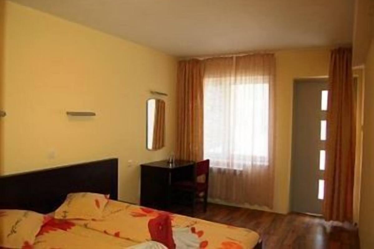 A hotel room with a bed, a desk, a chair, and a window with curtains.