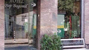 L’entrée d’un hôtel, avec une porte en verre, un pot de fleurs et un banc à l’extérieur.
