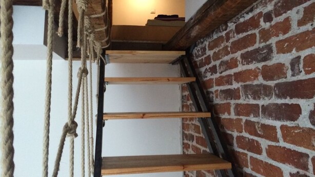 Un escalier en bois, avec un mur de briques d’un côté et une échelle de corde de l’autre.