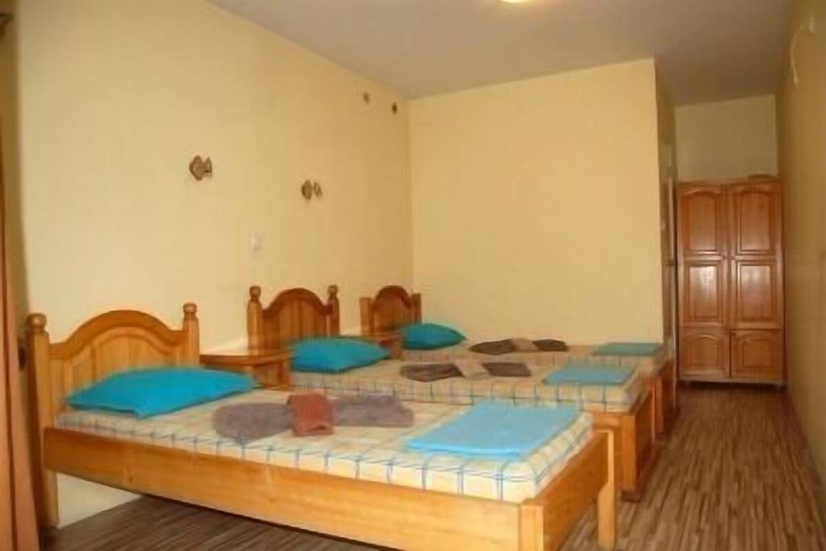 A room with two wooden beds, each with a blue and brown pillow, and a wooden wardrobe in the corner.