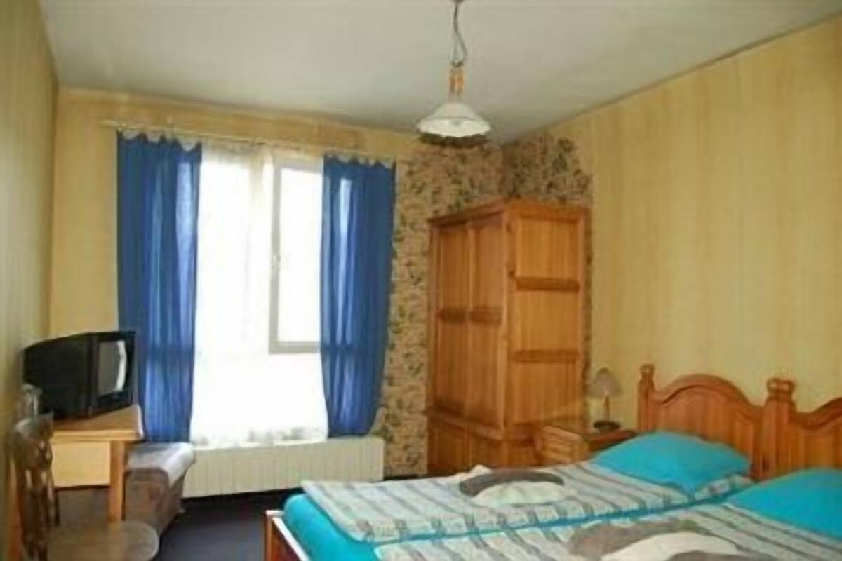 A bedroom with a bed, a wooden wardrobe, a television on a desk, and a window with curtains.