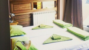 Une chambre à coucher avec une tête de lit en bois, un radiateur, une fenêtre avec des rideaux et des serviettes vertes soigneusement pliées sur le lit.
