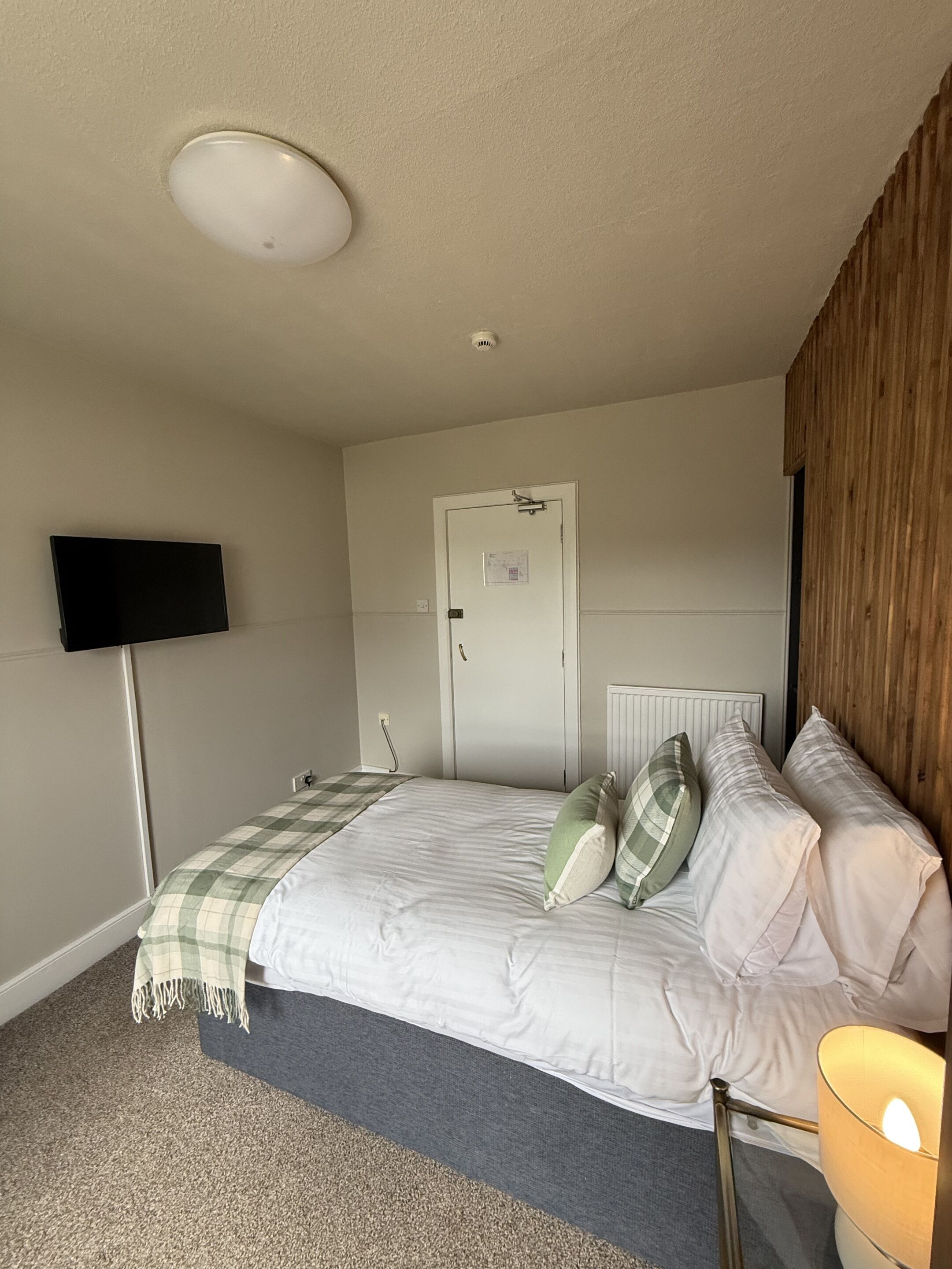 A bedroom with a bed, a television mounted on the wall, a door, and a radiator.