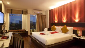 Habitación de hotel con una cama grande, un escritorio con silla, una mesa de comedor con fruta y vistas a la ciudad desde la ventana.
