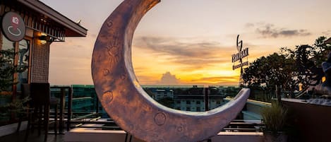 A crescent moon sculpture on a rooftop terrace with a sunset view.