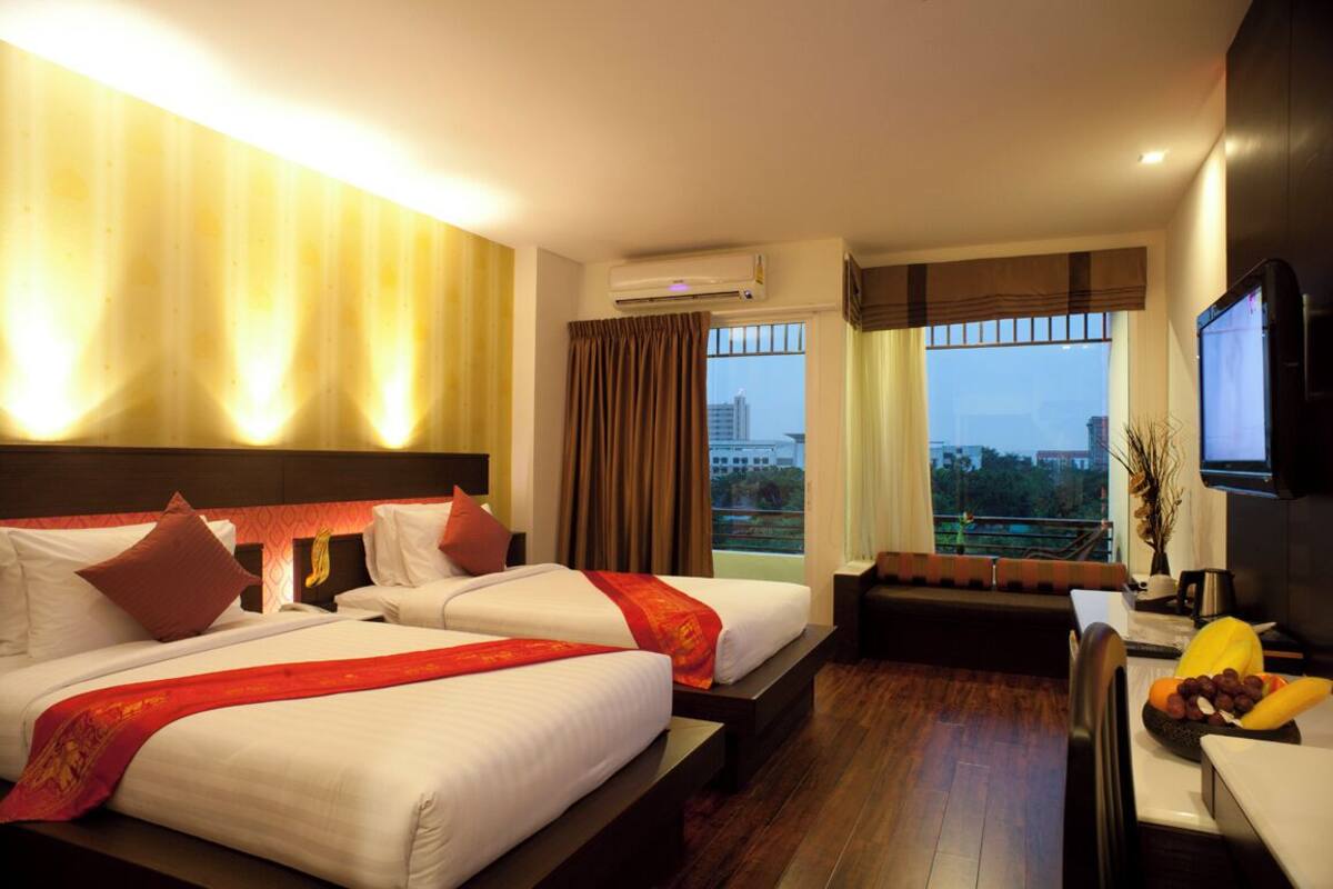 A hotel room with two beds, a sofa, a TV, and a view of the city.
