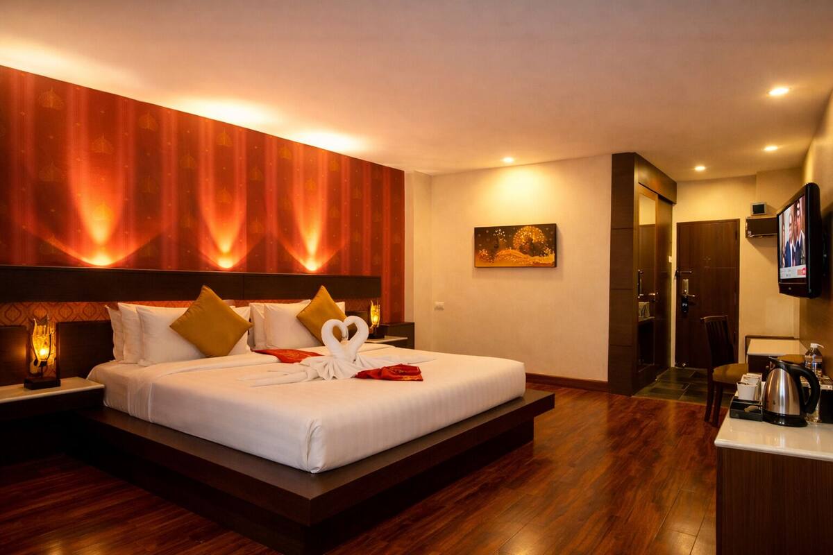 A hotel room with a large bed, a television, a desk with a coffee maker, and a painting on the wall.
