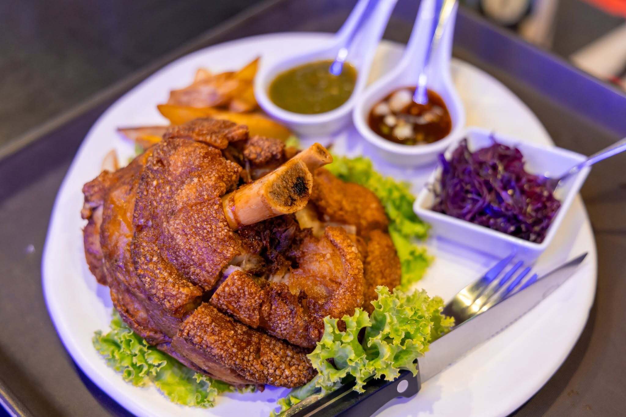 A plate with a roasted chicken leg, fries, and two dipping sauces.