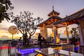An outdoor dining area with tables and chairs, a tree, and a gazebo structure. - Suvarnabhumi Suite (Bangkok)