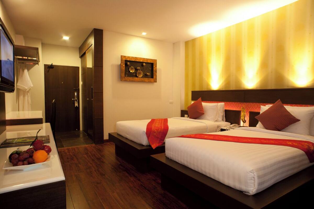 A hotel room with two beds, a TV, a desk with a fruit bowl, and a framed picture on the wall.