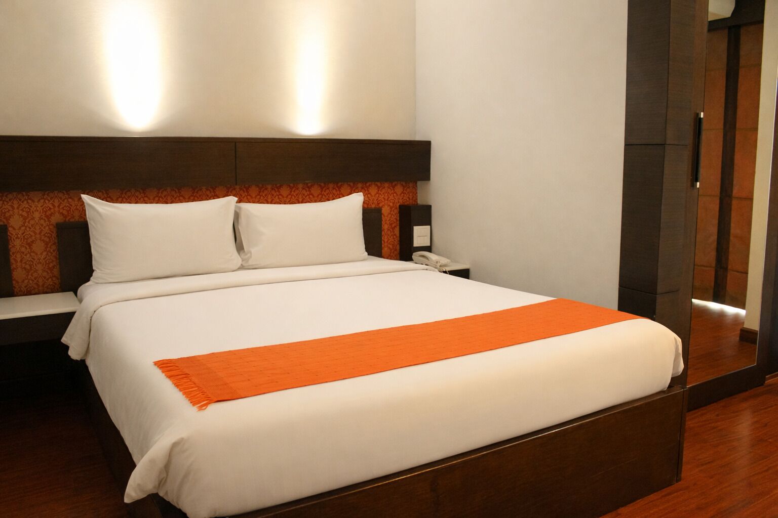 Una habitación de hotel con cama, mesita de noche, teléfono y espejo.