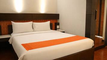 Una habitación de hotel con cama, mesita de noche, teléfono y espejo.