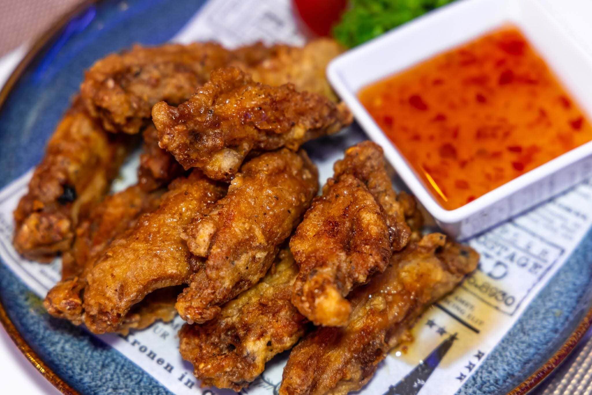 A plate of fried chicken wings with a side of dipping sauce.
