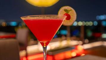 Un cóctel en una copa de martini con una cereza, sobre una mesa con una luna de fondo.