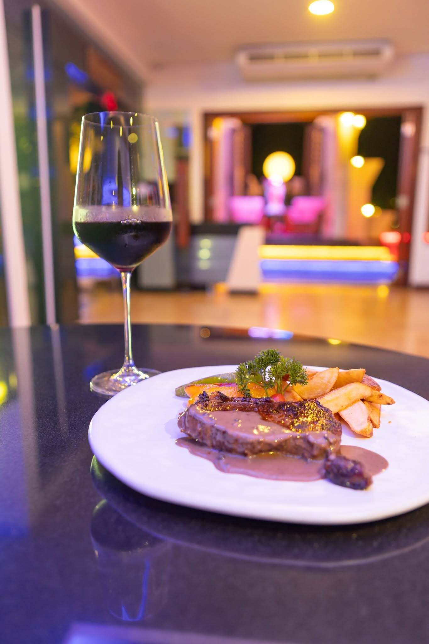A plate of food with a glass of red wine on a table in a well-lit room with a modern interior.