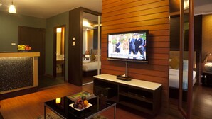 Une chambre d’hôtel équipée d’une télévision, d’une petite table avec un panier de fruits, d’un canapé et d’un lit.