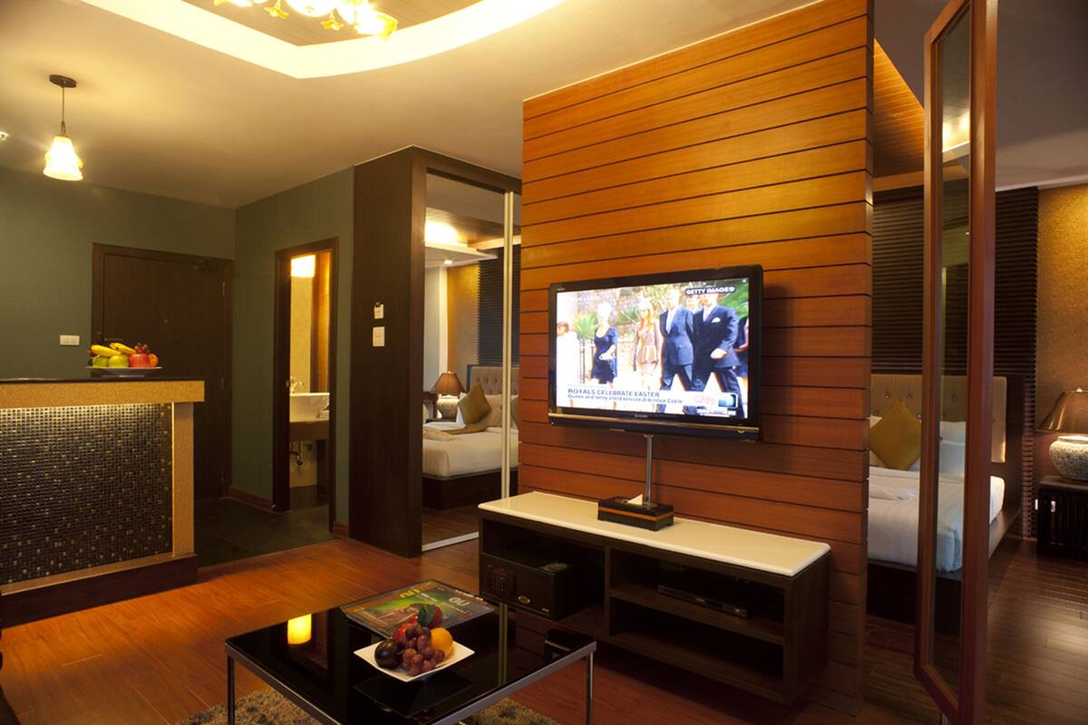 A hotel room with a television, a small table with a fruit bowl, a sofa, and a bed.