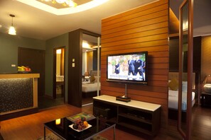 A hotel room with a television, a small table with a fruit bowl, a sofa, and a bed. - Suvarnabhumi Suite (Bangkok)