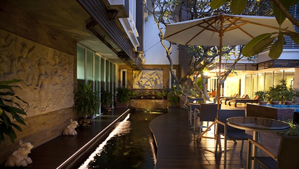 Un jardín interior tranquilo con fuente, zonas de estar y un mural en la pared.