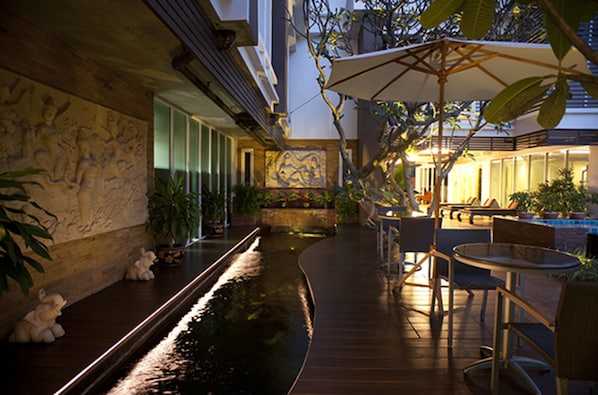 Un jardín interior tranquilo con fuente, zonas de estar y un mural en la pared.