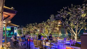 Un espace de restauration en plein air, avec des tables et des chaises, entouré d’arbres et éclairé par un éclairage d’ambiance.