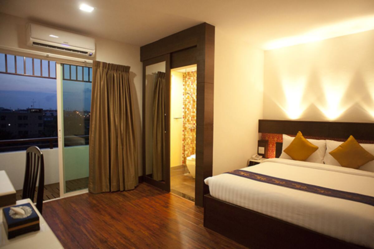 A hotel room with a bed, a nightstand, a desk with a chair, and a window with curtains.