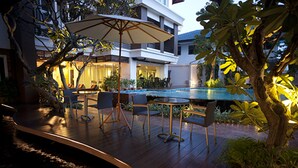 Un área junto a la piscina con terraza de madera, asientos al aire libre y vista a un edificio con balcones.