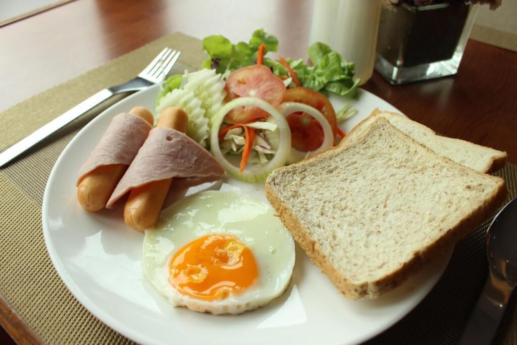 Un plato con huevos, jamón, pan y una ensalada.