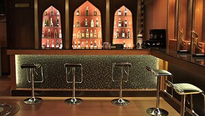 Un área de bar con tres taburetes, una barra con salpicadero de azulejos y una exhibición de botellas detrás de un ventanal emplomado.