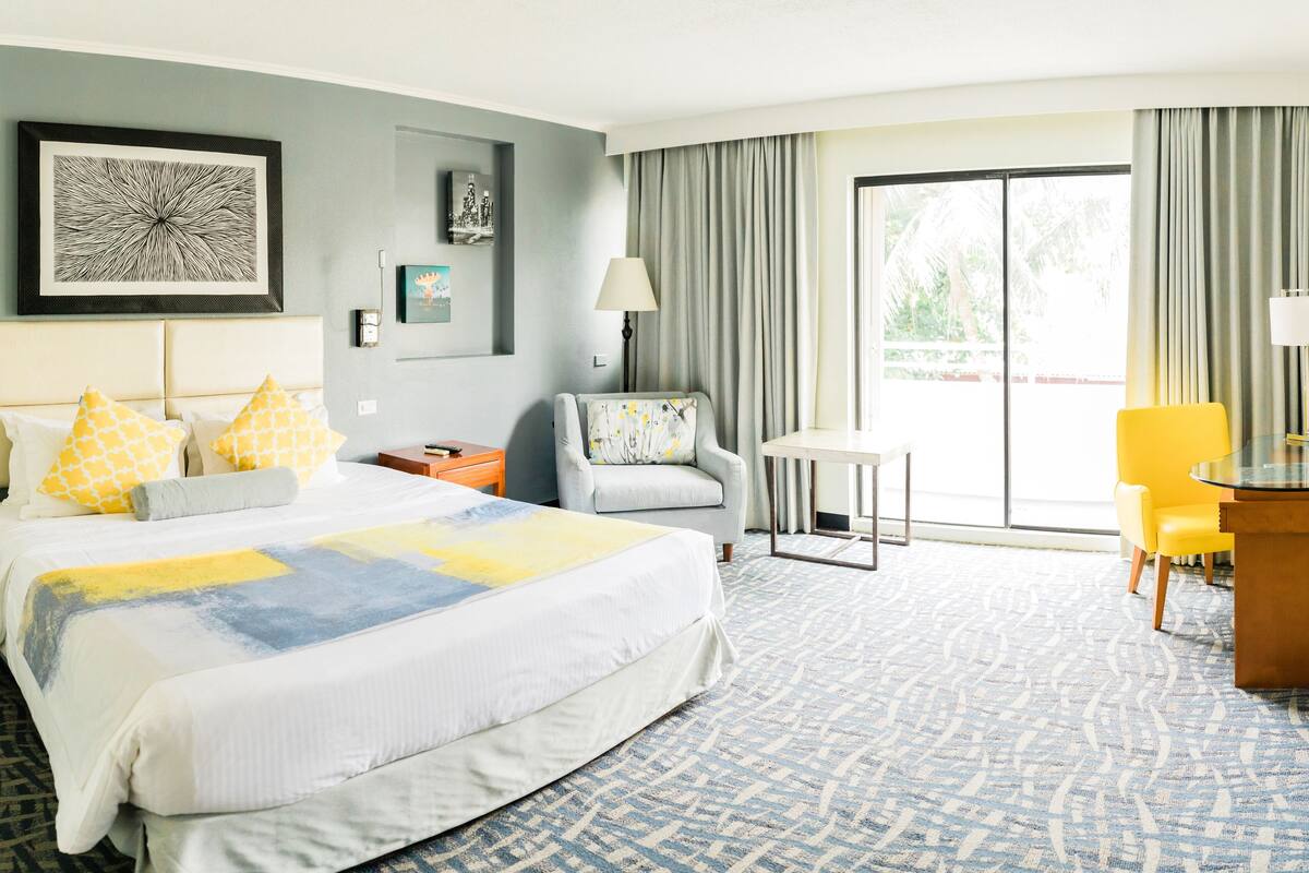 A hotel room with a large bed, a chair, a small table, and a desk.