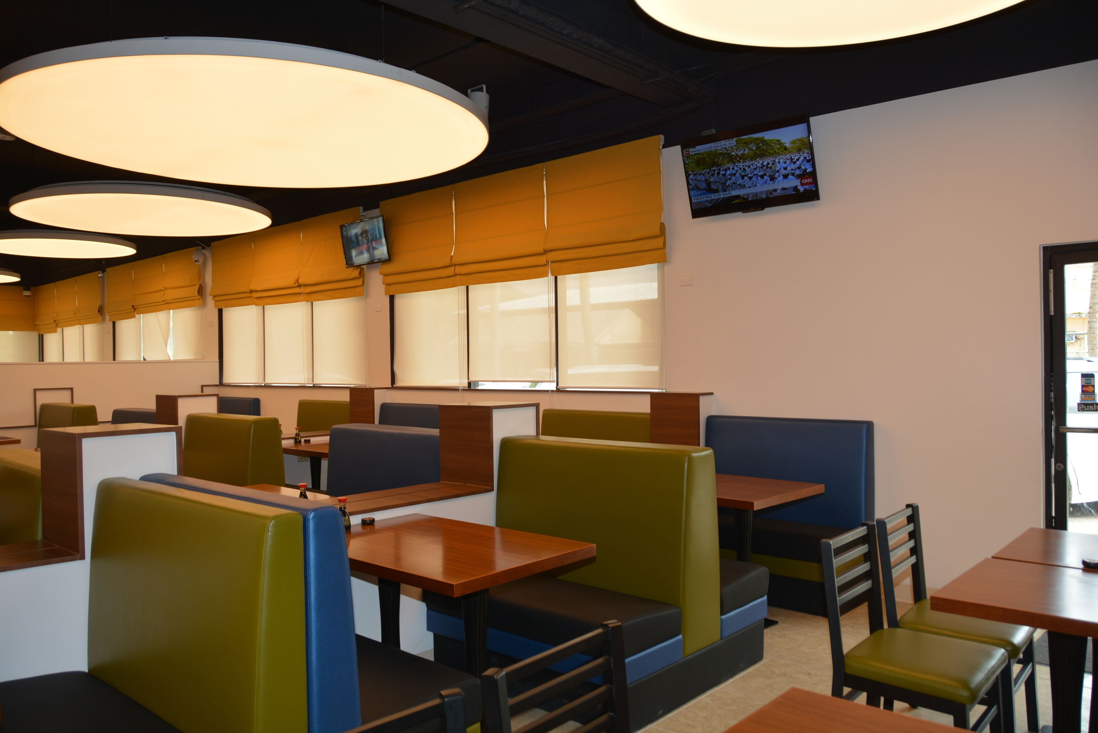 A restaurant with booths and tables, large overhead lights, and a TV on the wall.