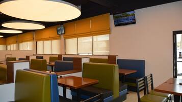 A restaurant with booths and tables, large overhead lights, and a TV on the wall.